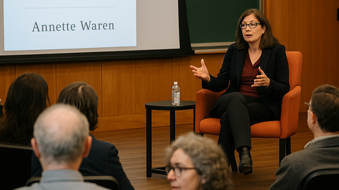 An author discusses her book in a university setting, seated in front of a screen showing the book title to a small audience.